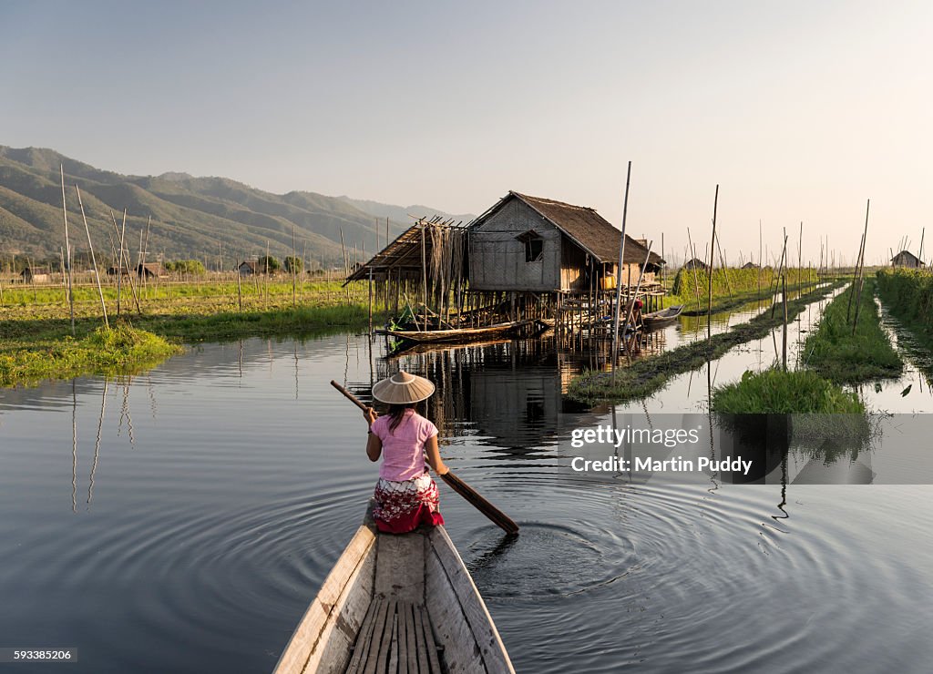Myanmar, woman rowing boat towards house on stilts on Inle lake