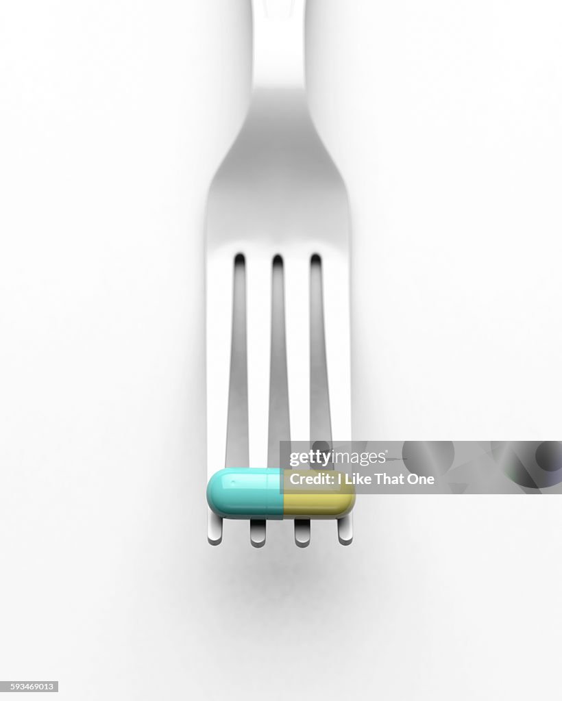 White plastic fork holding a green and yellow pill