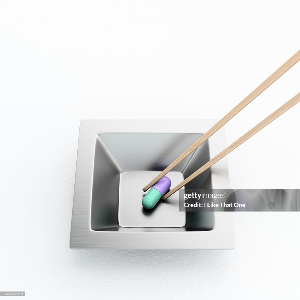 Pill in a steel cup being lifted by chopsticks