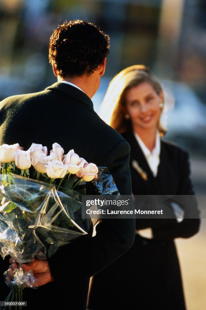 Couple, rear view of man hiding bouquet of roses behind back