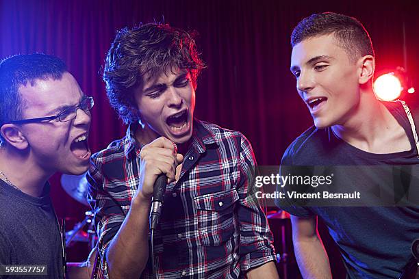 three teenager singing into a microphone on stage - boy singing stock-fotos und bilder