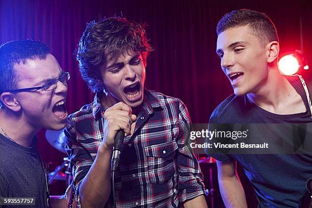 three teenager singing into a microphone on stage - boy band stockfoto's en -beelden