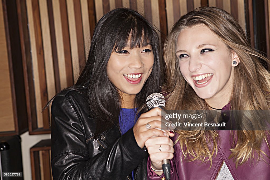 Two young girls singing into a microphone