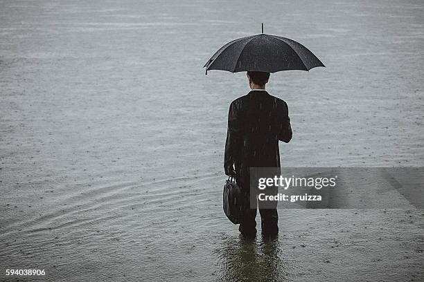 handsome man wearing suit and holding umbrella during the rain - business flood stock pictures, royalty-free photos & images