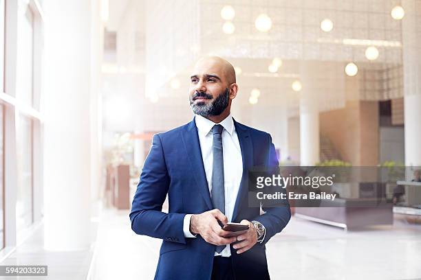 businessman looking out a window in modern office - geschäftsmann im büro mobiltelefon stock-fotos und bilder