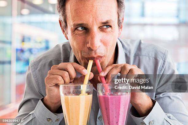 man drinking from two smoothies - avarice fotografías e imágenes de stock