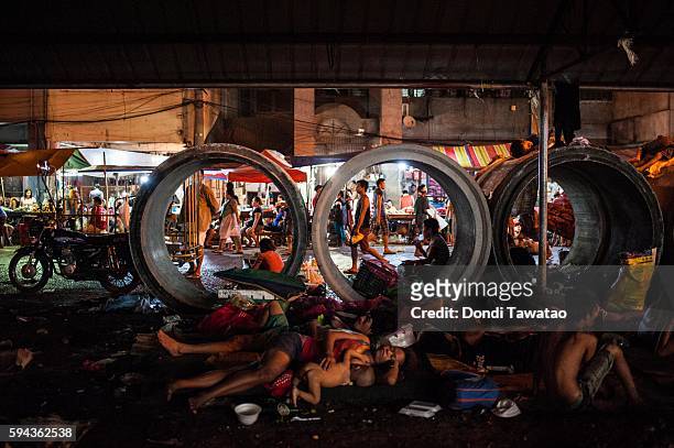 Vendors and porters work in the background while homeless people sleep on the pavement in a working class district on August 19, 2016 in Manila,...