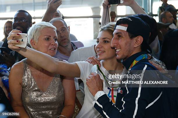 French boxer and silver medallist Sofiane Oumiha shows his medal as he poses for a photograph with a fan at the Roissy-Charles-De-Gaulle airport as...