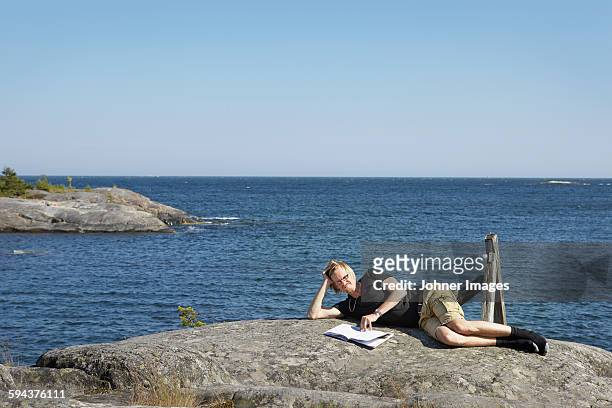 woman with book on rock at sea - lying on side stockfoto's en -beelden