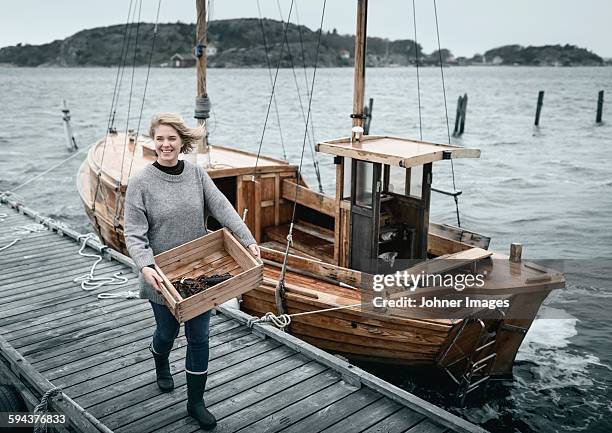 smiling woman carrying lobsters, boat on background - grebbestad stockfoto's en -beelden