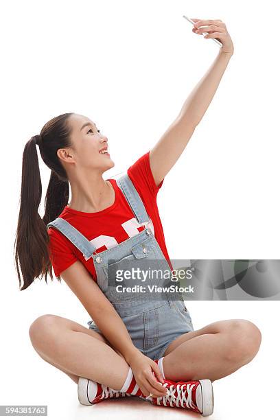 young woman taking a picture of herself with a mobile phone - sitting and using smartphone studio stockfoto's en -beelden