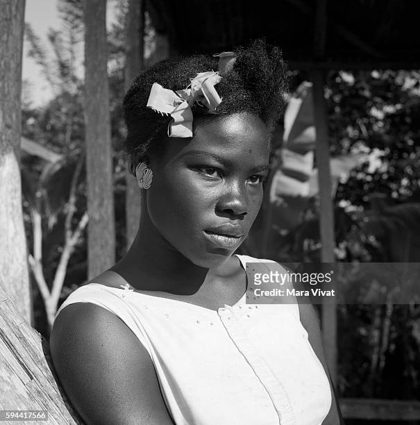 Teenage girl wearing a ribbon in her hair, leans against a tree on Jamaica.
