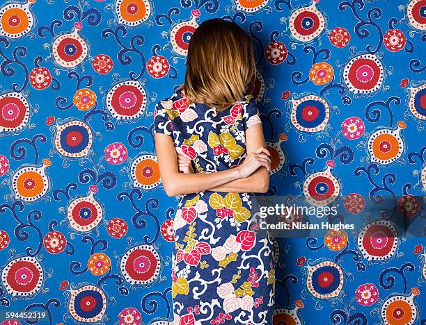 woman wearing print dress against print background - floral pattern dress stock-fotos und bilder