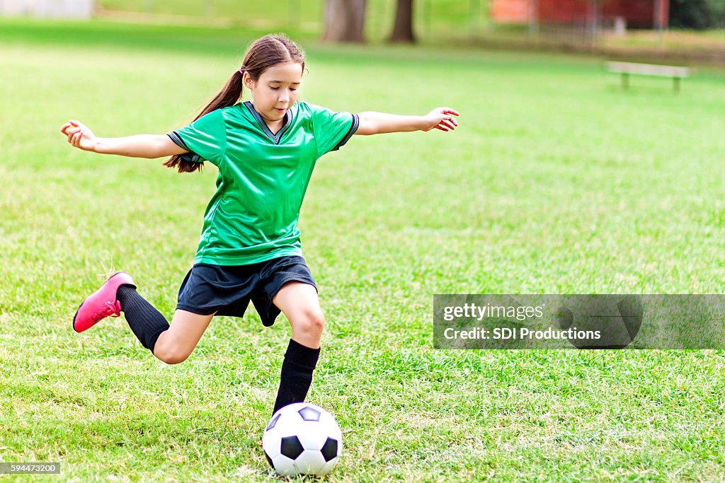 Intense Hispanic preteen girl kicks soccer ball