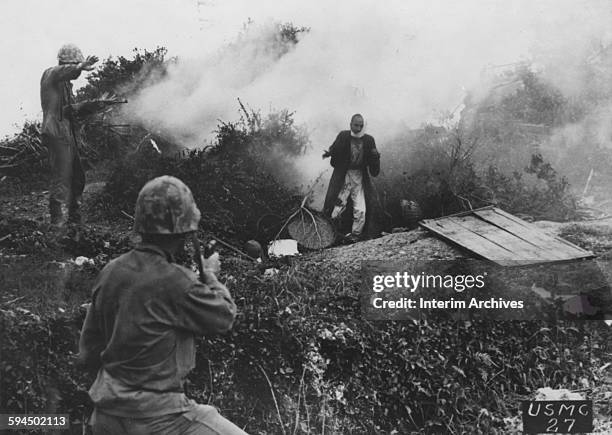 Marine rifleman signals his companions to hold their fire as a Japanese soldier emerges from a cave in Okinawa, 1945. Persuaded by a smoke grenade,...