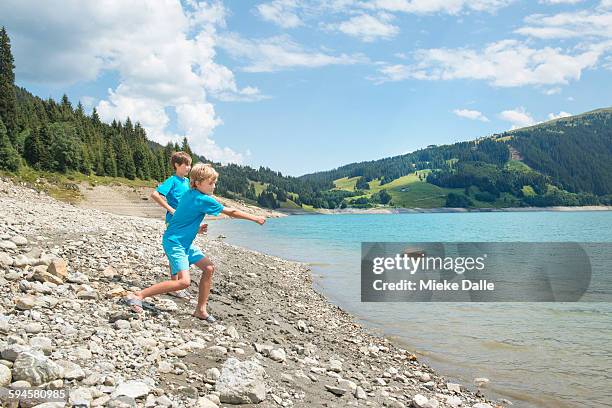 boys skimming stones into lake in austria - boy throwing stock-fotos und bilder