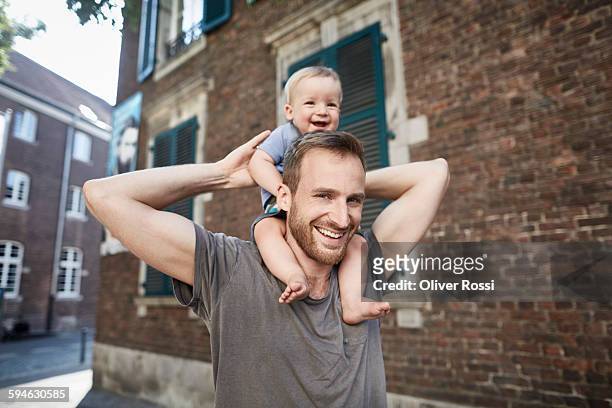 smiling father carrying baby on shoulders - leanincollection father stock-fotos und bilder