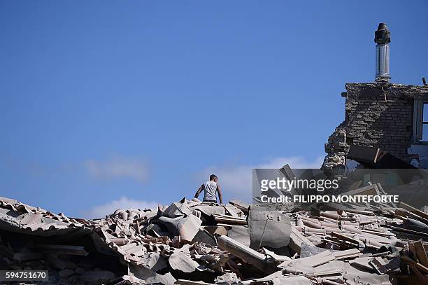 Man sits on top of rubble in Amatrice on August 24, 2016 after a powerful earthquake rocked central Italy. The earthquake left 38 people dead and the...