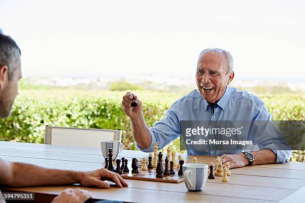 smiling senior man playing chess with son - senior playing chess stock pictures, royalty-free photos & images