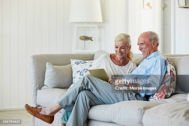 smiling senior couple using digital tablet at home - 80s living room fotografías e imágenes de stock
