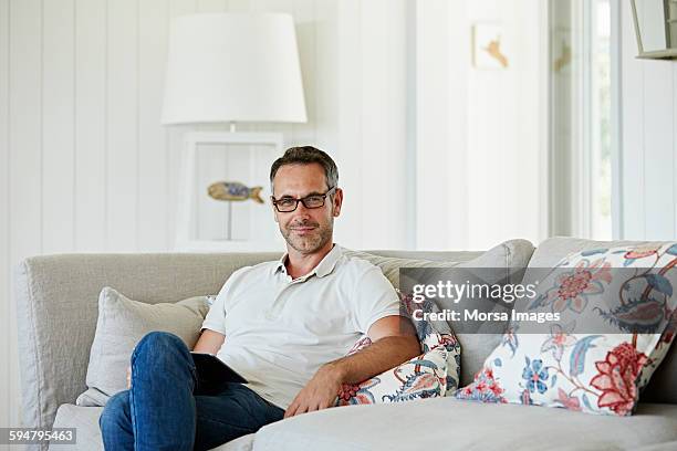 man with digital tablet sitting on sofa - polo shirt stock pictures, royalty-free photos & images