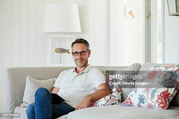 man with digital tablet sitting on sofa - camisa pólo imagens e fotografias de stock