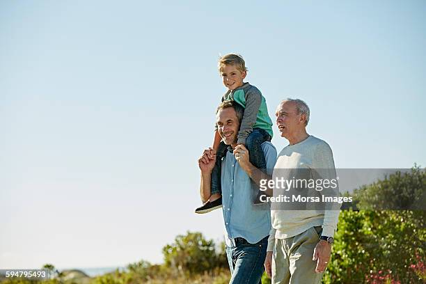 happy three generation males walking on field - mann mit kind auf den schultern stock-fotos und bilder
