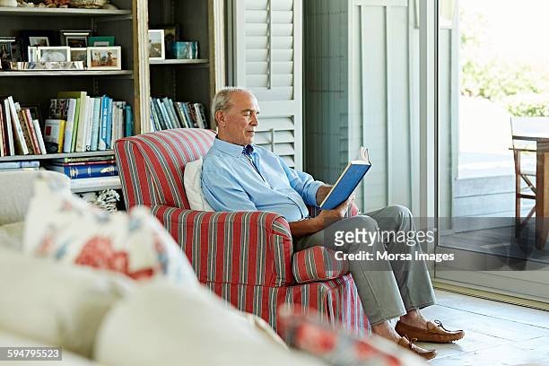 senior man reading book on chair - 80s living room fotografías e imágenes de stock
