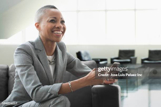 black businesswoman using cell phone on sofa in office - business people authentic stockfoto's en -beelden