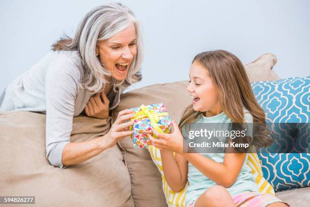 caucasian girl giving grandmother a gift in living room - child giving gift stock-fotos und bilder