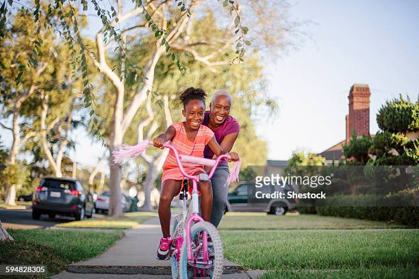 mother pushing daughter on bicycle - fahrrad fahren großeltern mit kind stock-fotos und bilder