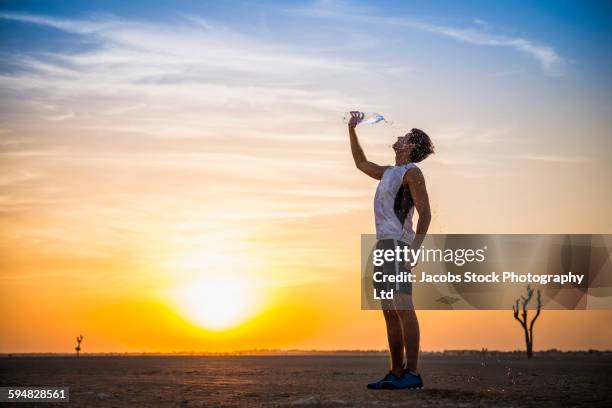 caucasian man pouring water bottle on himself in desert - arabische muster stockfoto's en -beelden