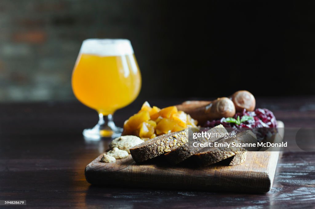 Bread, fruit and cheese on cutting board with beer