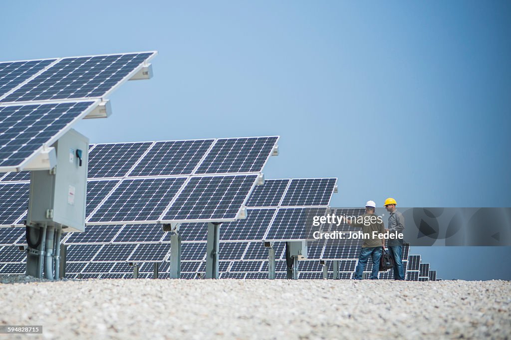 Caucasian technicians talking near solar panels