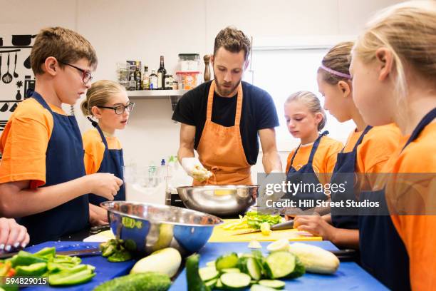 teacher and students chopping vegetables in cooking class - children cooking school stock-fotos und bilder