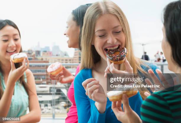 women eating donuts on urban rooftop - friends donut stock-fotos und bilder