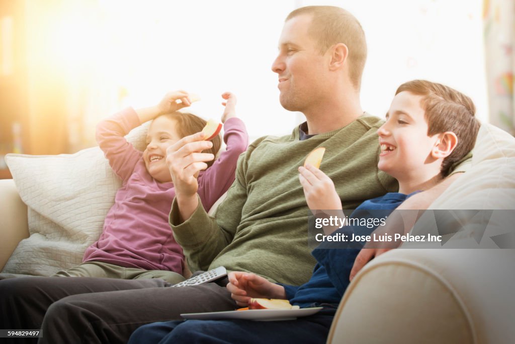 Caucasian father and children eating snacks on sofa