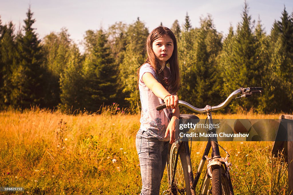 Caucasian teenage girl pushing bicycle in field