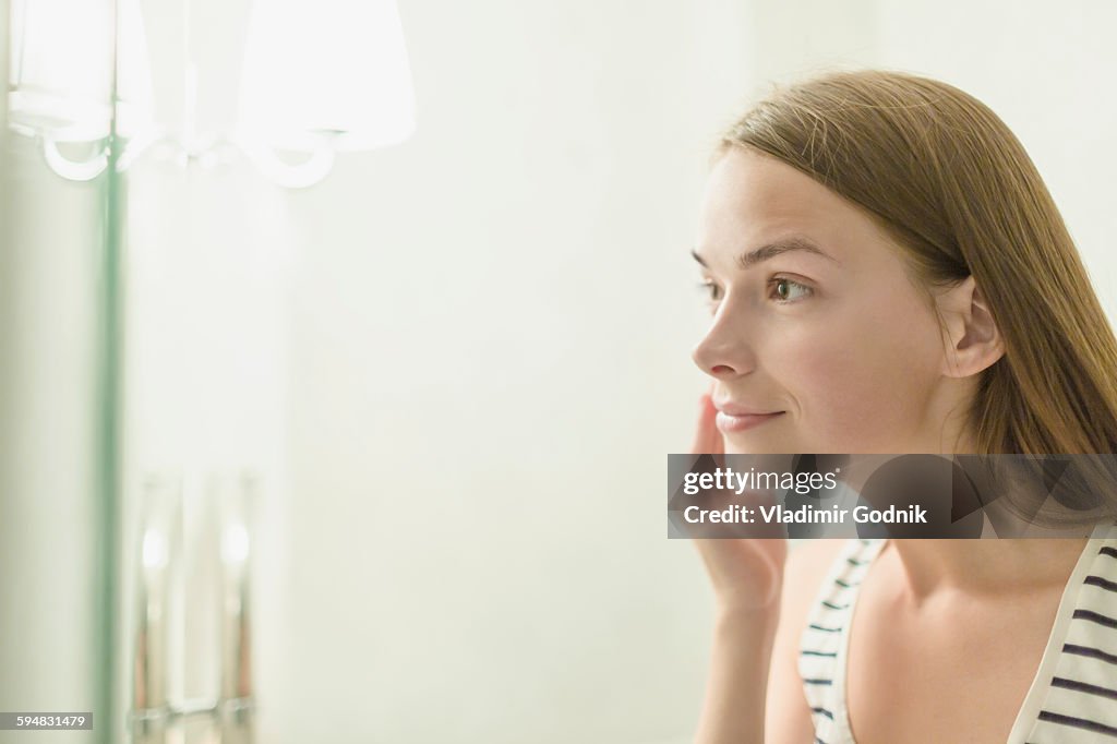 Beautiful woman applying cream on face in domestic bathroom