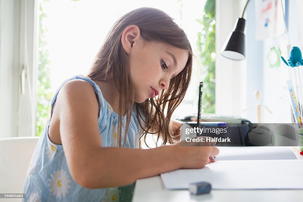 Side view of girl writing in book on table at home