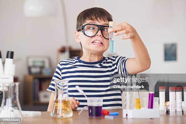 cross eyed boy looking at test tube during science experiment in house - uitvinder stockfoto's en -beelden