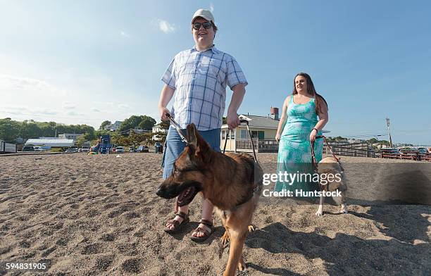 blind couple with their service dogs walking along the beach - love is blind stock-fotos und bilder