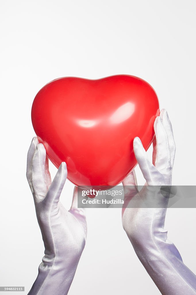 Cropped hands of bride holding heart shape balloon against white background