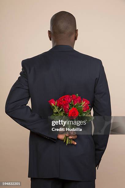 rear view of well-dressed man holding roses against colored background - mãos-atrás-das-costas imagens e fotografias de stock