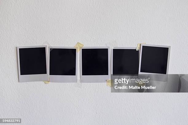 blank instant camera prints stuck on white wall - polaroids stock-fotos und bilder