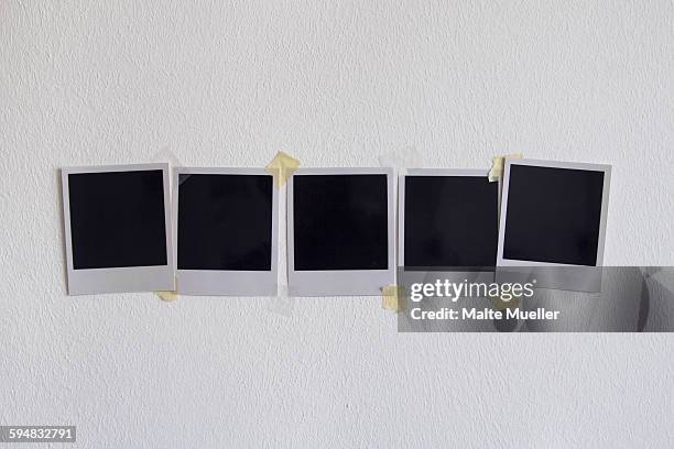 blank instant camera prints stuck on white wall - transferência de impressão instantânea imagens e fotografias de stock