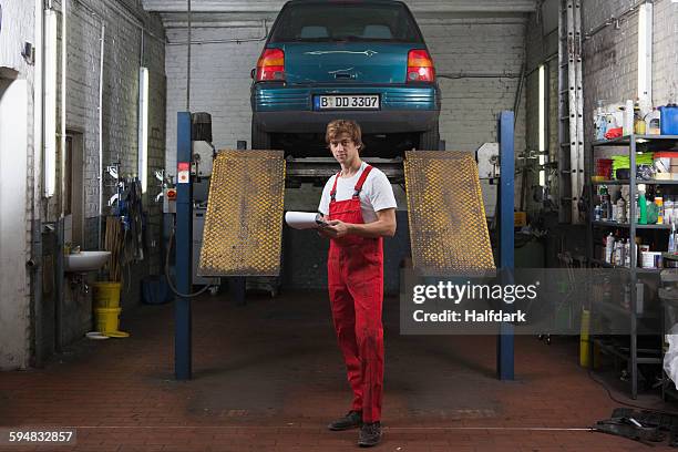 portrait of confident mechanic holding clipboard at garage - dungarees stock-fotos und bilder