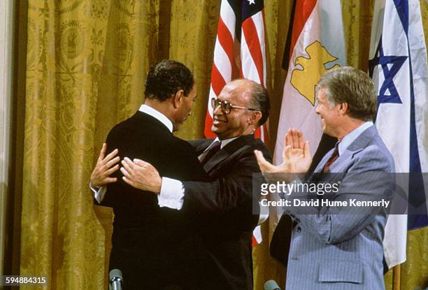 Egyptian President Anwar al-Sadat and Israeli Premier Menachem Begin embrace, while US President Jimmy Carter applauds after signing the Camp David...