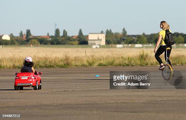 Child drives a toy car as a woman rides a unicycle at the former Tempelhof airport on August 24, 2016 in Berlin, Germany. In a sudden change of...