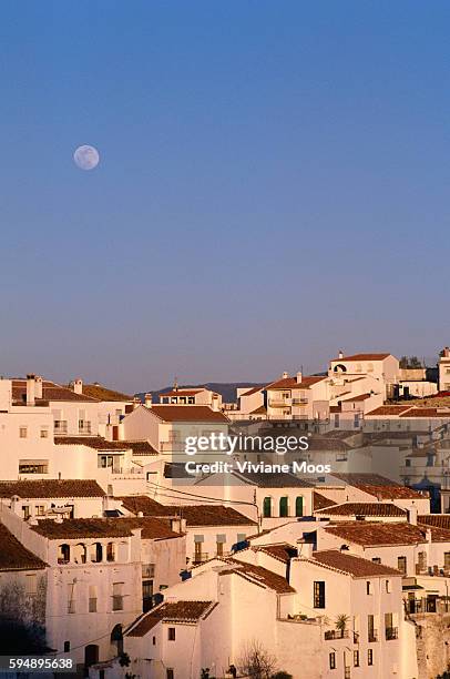 Overhead view of white, tiled roof houses in Gaucin, Spain. The moon can be in the sky above.